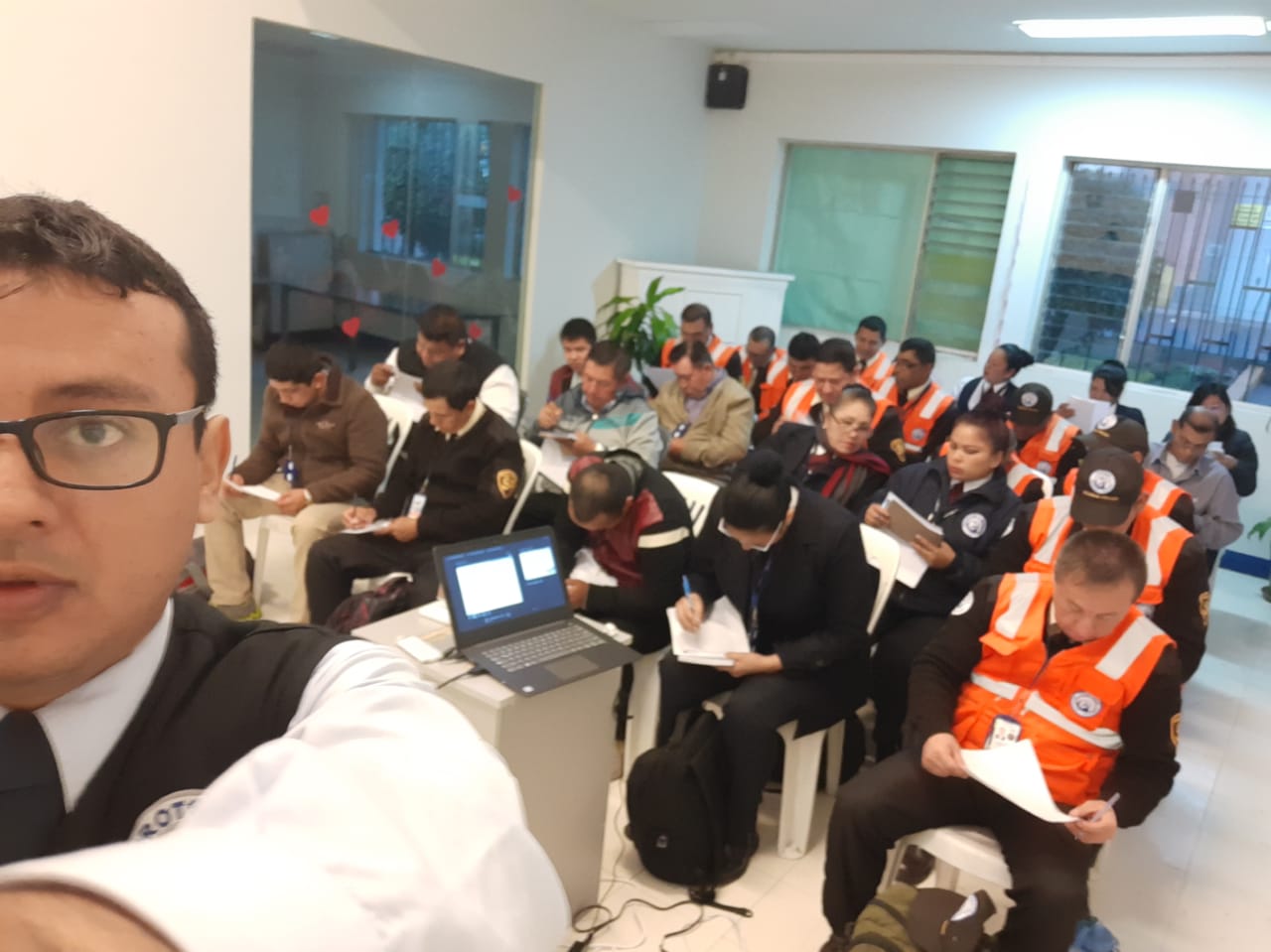 Aula con personal de vigilancia en chalecos naranjas atendiendo una capacitación presencial